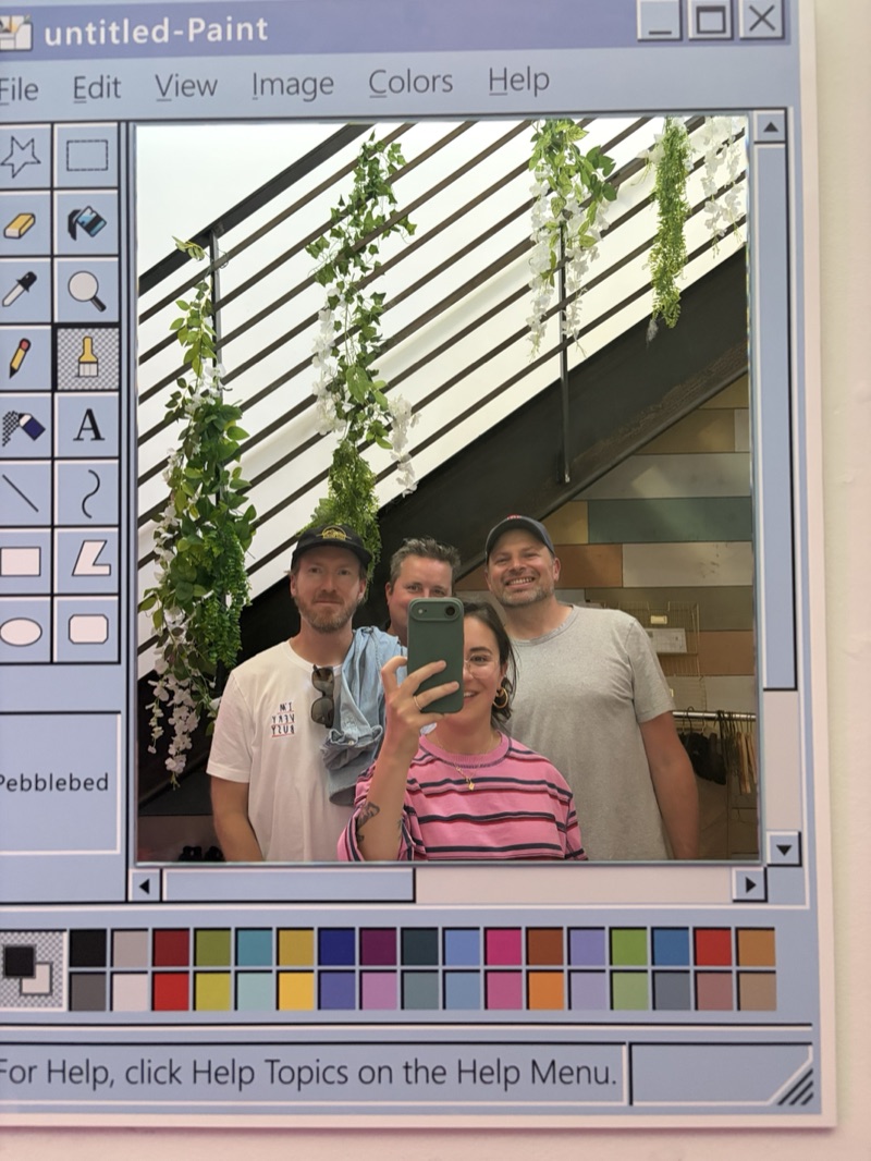 Johnny, Jamie, Anna and Myles taking a mirror selfie, framed in an old Paint window.